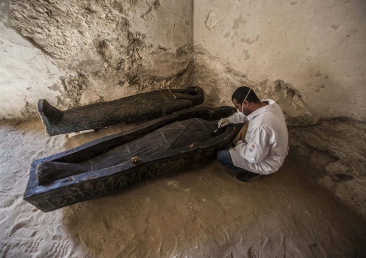 The Egyptian archaeologist brushes a mummy into a black carved wooden sarcophagus inlaid with gilded leaves. Discovered between the Royal Tombs of the Valley of the Queens and the Valley of the Kings.