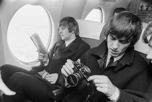 Beatles Ringo Starr and George Harrison on a plane with book and camera by Morrie Hill courtesy ATL